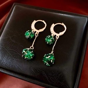 Detail of emerald green tassels and gold earrings displayed on a luxury black jewelry box