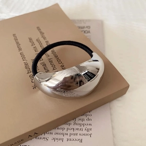 Minimalist silver metal crescent hair tie with elastic rope on vintage newspaper background