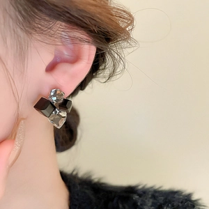 Close-up of geometric square crystal earrings worn on ear showing faceted details