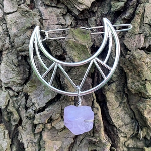 Close-up of hollow moon hair clip with purple crystal stone on natural bark background