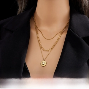 Detailed close-up of layered gold necklace with paperclip chain and coin pendant charm