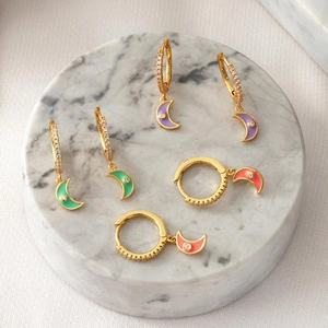 Three pairs of gold crescent moon hoop earrings with purple, green, and pink enamel charms