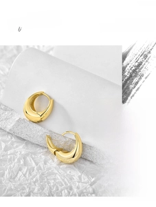 Macro shot of high-polished gold-plated crescent hoop earrings on elegant white textures