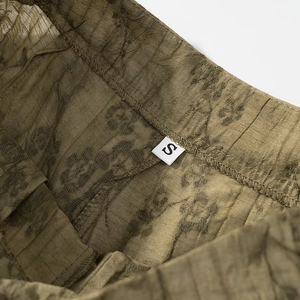 Macro detail of size S tag on olive green jacquard fabric trousers with textured pattern