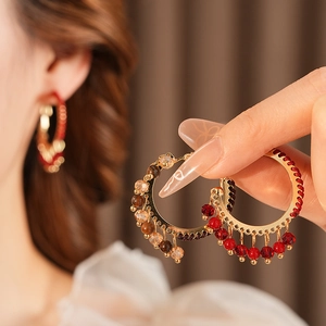 Dettaglio di orecchini a cerchio stile vintage con corde rosse e ciondoli a perline