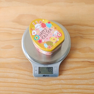 Close-up of Easter egg tin box on a scale showing a weight of approximately 70 grams