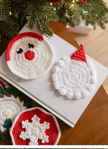 Detailed view of hand-knitted Christmas coasters with Santa and tree motifs on a wooden table