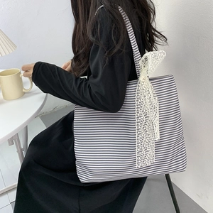 Detailed side view of large canvas tote bag with black stripes and lace bow detail