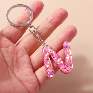 Close-up of pink glitter letter N keychain made of resin with shiny gold flakes