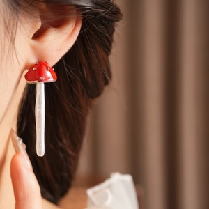 Detail of a red mushroom earring with white dots on a model against a warm background