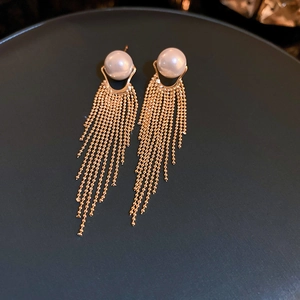 Detailed view of long gold tassel earrings featuring elegant white pearls on a dark tray