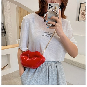 Close-up of red lip-shaped crossbody bag in glossy patent leather with gold chain strap