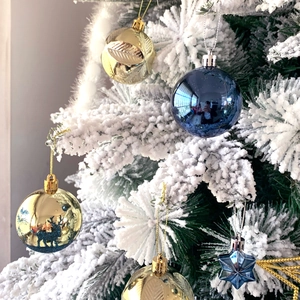 Detail of blue and gold Christmas ornaments including stars and globes on snowy tree