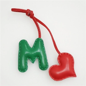Close-up of handmade green leather letter M and red heart charm with visible stitching