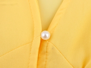 Detailed macro view of a V-neckline on a yellow dress featuring a white pearl button
