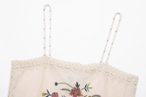 Detail of beige cotton camisole featuring floral embroidery, lace trim and braided straps