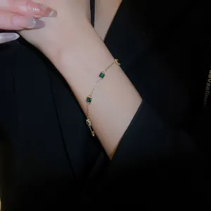 Gros plan d'un bracelet doré avec pierres carrées vert émeraude et bordure perlée rétro