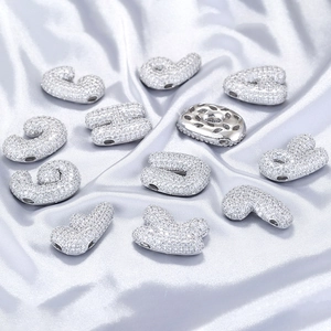 Macro shot of silver paved cubic zirconia alphabet pendants on soft silk fabric background