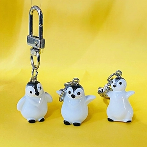 Detailed close-up of three cute 3D resin penguin keychains in various poses on yellow background