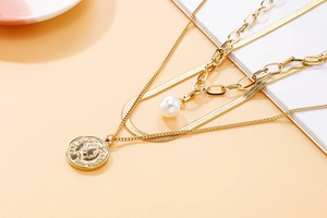 Détail du collier multicouche doré avec perle baroque et pendentif pièce en relief