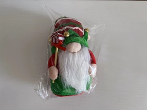 Detailed view of Christmas gnome plush with red-green hat, white beard and bell in packaging