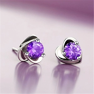 Macro shot of silver heart earrings featuring round purple gemstones in a prong setting