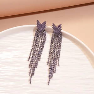 Macro shot of V-shaped purple rhinestone tassel earrings on a white ceramic plate