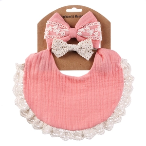 Close-up of pink muslin baby bib with beige lace trim and matching bow headbands