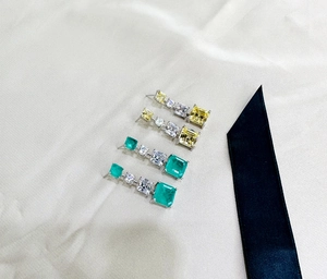 Macro detail of square emerald and yellow sapphire earrings on gold satin fabric