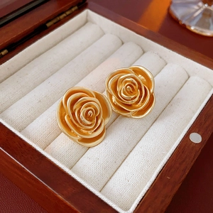 Nahaufnahme eleganter goldener Rosenohrringe mit strukturierten Blüten in einer Holzbox