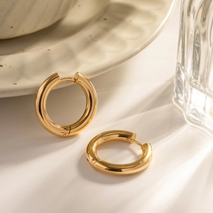 Macro shot of double-layer gold hoop earrings on ceramic plate with elegant lighting