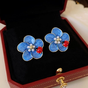 Blue enamel flower earrings with gold edges and red ladybug in a red jewelry box