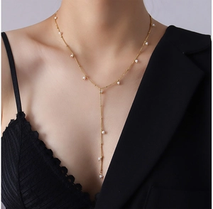 Detail of golden Y-shaped long necklace with pearls on a model wearing black V-neck top
