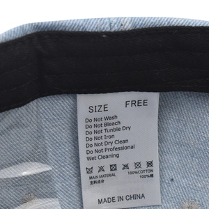 Detail of internal care label on washed denim baseball cap showing 100% cotton material