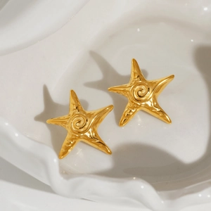 Close-up of gold starfish earrings with spiral texture on white ceramic plate
