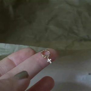 Close-up of a small gold hoop earring with a sparkling cross pendant held by hand