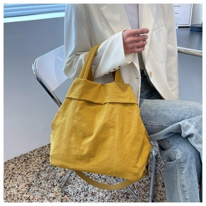 Detail of a large yellow nylon tote bag styled with a white blazer in a modern setting