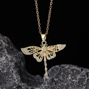 Macro shot of gold dragonfly pendant with white zircons and green gemstone eyes