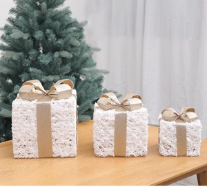 Three tiered white glitter Christmas gift boxes with gold ribbons and LED lights on wood table