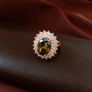 Detail of oval olive green gemstone ring with pavé crystals on dark leather surface