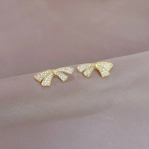 Boucles d'oreilles nœud dorées avec cristaux pavés sur fond de velours violet doux