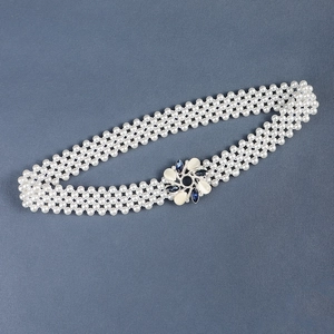 Close-up of pearl waist belt featuring a floral buckle with blue and white gemstones