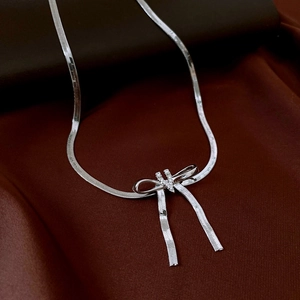 Detail of silver snake chain necklace with zircon bow pendant on brown silk background