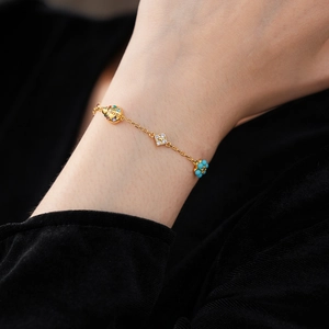Detail of ladybug and flower charms on a turquoise beaded golden bracelet for women