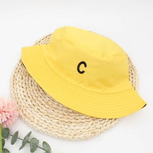 Detail of yellow cotton bucket hat featuring black letter C embroidery on a woven mat