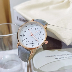 Dettaglio del cinturino in pelle grigia e orologio al quarzo oro rosa su un libro