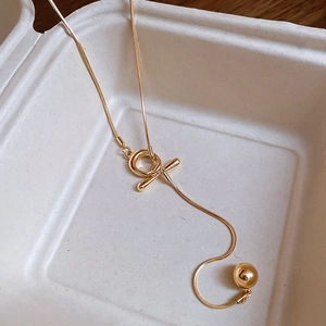 Detail of a minimalist gold snake chain necklace with toggle clasp and solid ball pendant