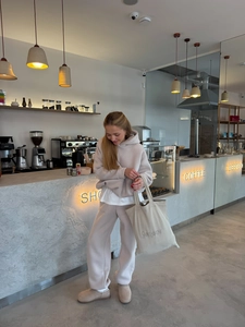 Beige dames set met hoodie en joggingbroek in een moderne koffiebar omgeving