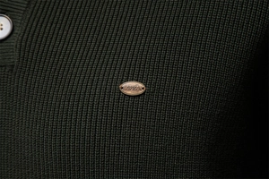 Close-up of dark green ribbed knit fabric with premium metal logo brand detail