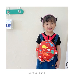 Toddler modeling a red mini backpack with colorful dinosaur prints and canvas texture